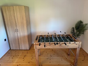 A wooden foosball table in a room with a wooden wardrobe and a potted plant.