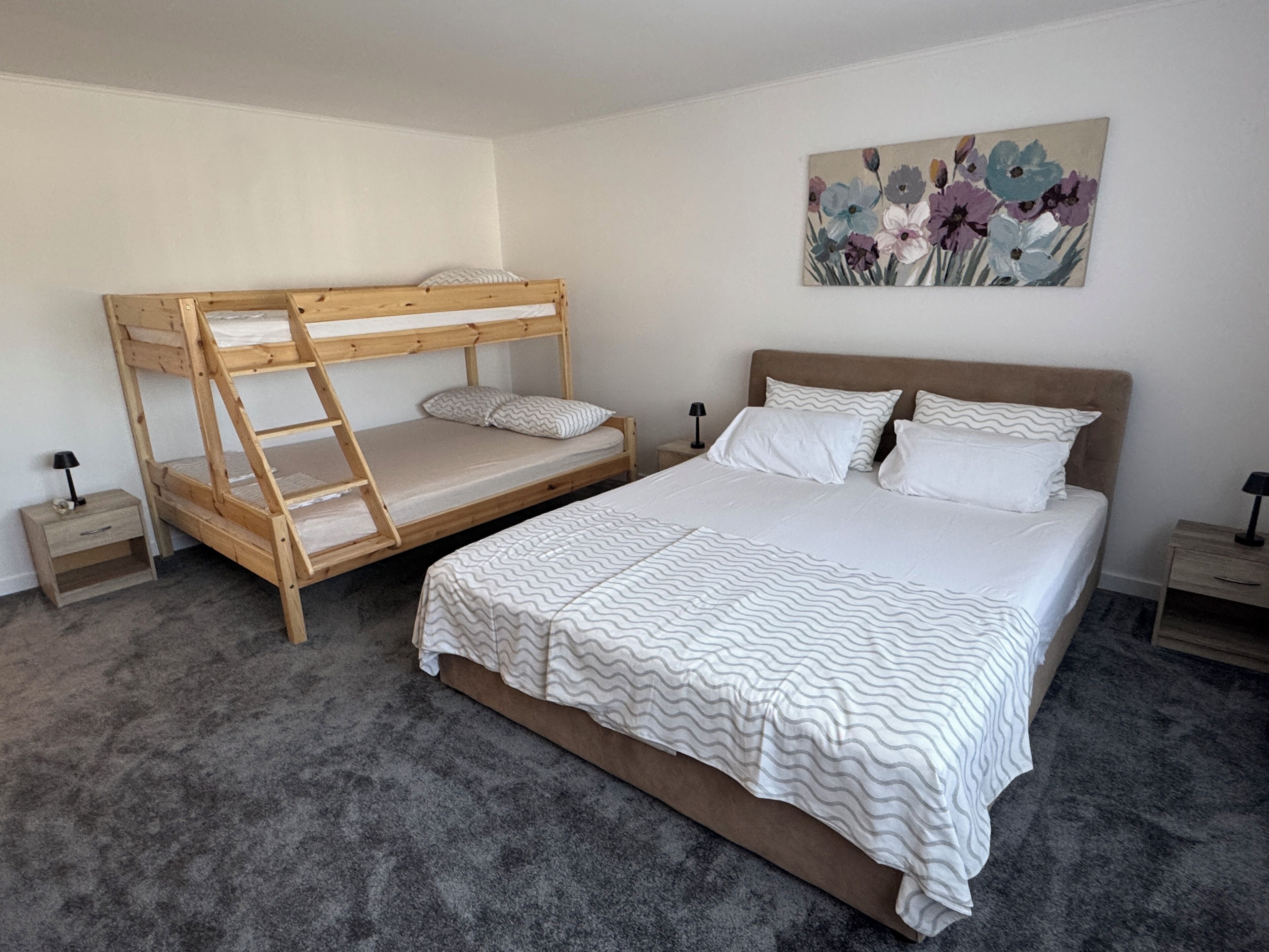 Ein Schlafzimmer mit Etagenbett, einem Einzelbett, einem Nachttisch, einer Lampe und einem Bild an der Wand.