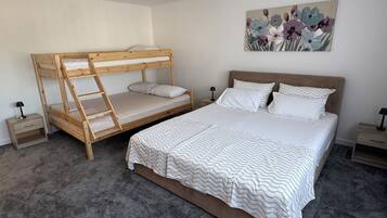 Ein Schlafzimmer mit Etagenbett, einem Einzelbett, einem Nachttisch, einer Lampe und einem Bild an der Wand.