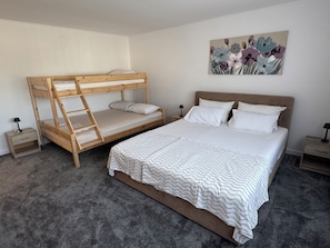 A bedroom with a bunk bed, a single bed, a nightstand, a lamp, and a painting on the wall.