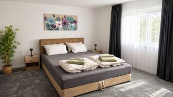 A bedroom with a large bed, a nightstand, a lamp, a potted plant, and a window with curtains.