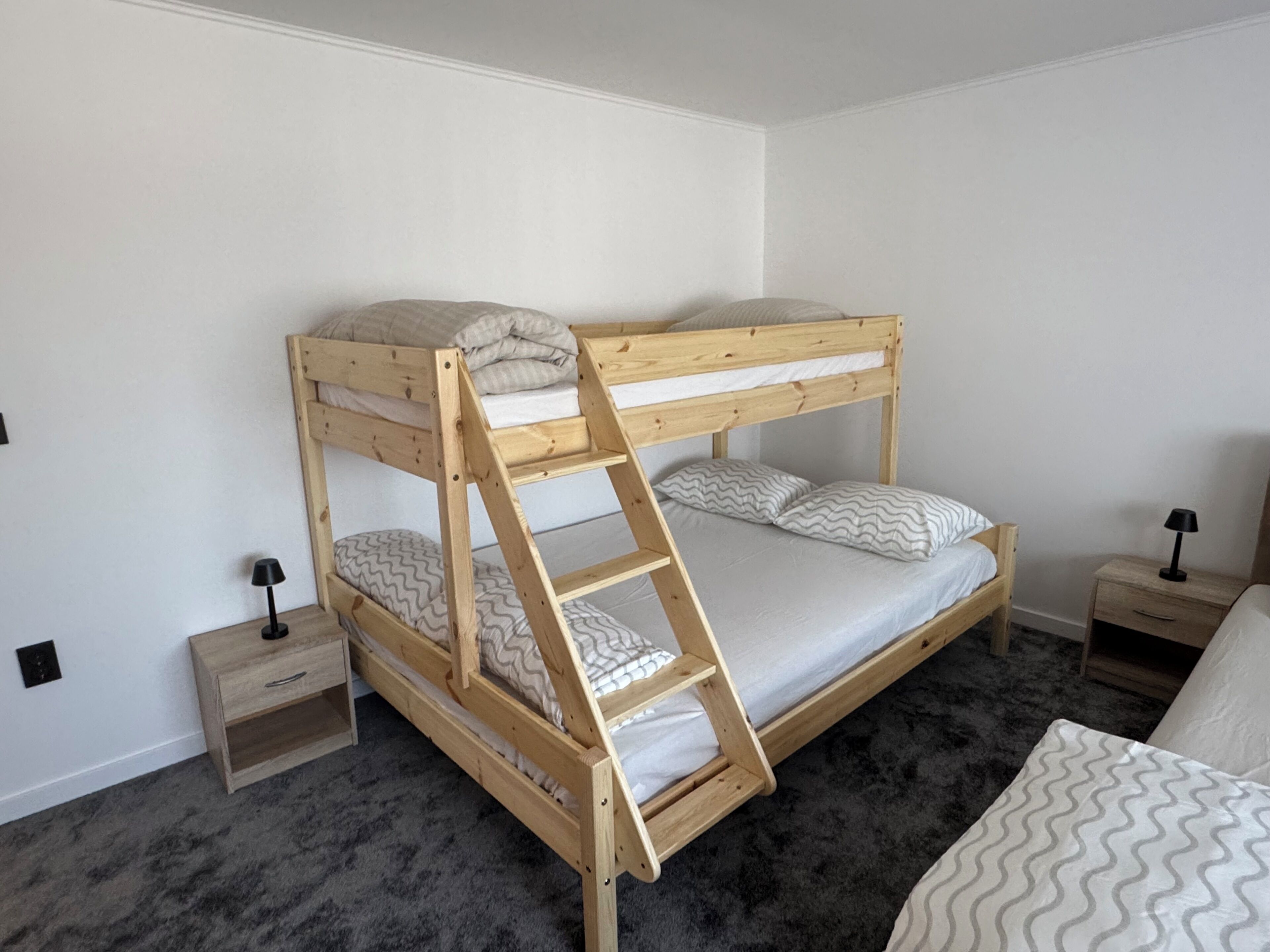 Una cama litera con escalera, una mesita de noche, un cajón y una lámpara.