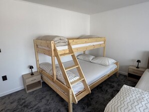A bunk bed with a ladder, a bedside table, a drawer, and a lamp.