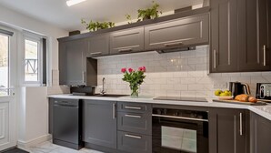 A modern kitchen with dark cabinets, a built-in oven, and a window with a view. - 3 Bed in Llandudno (oc-95068) (Llandudno)