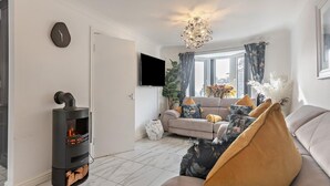 A modern living room with a fireplace, sofa, and a TV mounted on the wall. - 3 Bed in Llandudno (oc-95068) (Llandudno)