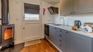 Een moderne keuken met een houtkachel, grijze kastjes, een raam met uitzicht en een bord met daarop een indicatie voor een branddeken.