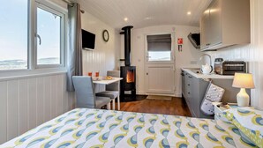 Een knus verblijf met een bed, een tafel met stoelen, een klein keukentje en een open haard.