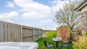 A hot tub with a wooden fence, a stone wall, and a small table with chairs in a backyard. - 1 Bed in Umberleigh (oc-82998) (Atherington)