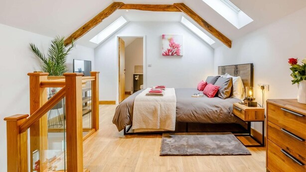 A bedroom with a sloped ceiling, wooden beams, a bed with pillows, a nightstand, a dresser, and a skylight. - 1 Bed in Umberleigh (oc-82998) (Atherington)