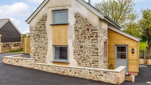 A stone building with a wooden door, a window, and a small porch area. - 1 Bed in Umberleigh (oc-82998) (Atherington)