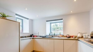 A modern kitchen with a wooden floor, white cabinets, a sink, and two windows. - 1 Bed in Umberleigh (oc-82998) (Atherington)