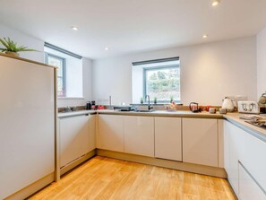 A modern kitchen with a wooden floor, white cabinets, a sink, and two windows. - 1 Bed in Umberleigh (oc-82998) (Atherington)