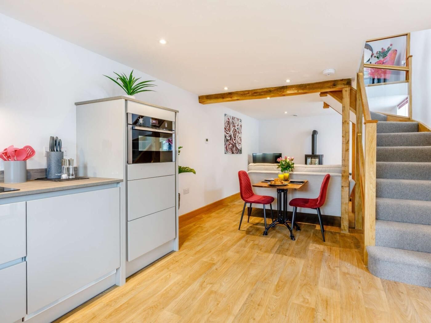 A compact kitchen with modern appliances, a dining area with two chairs, and a staircase leading to an upper level.