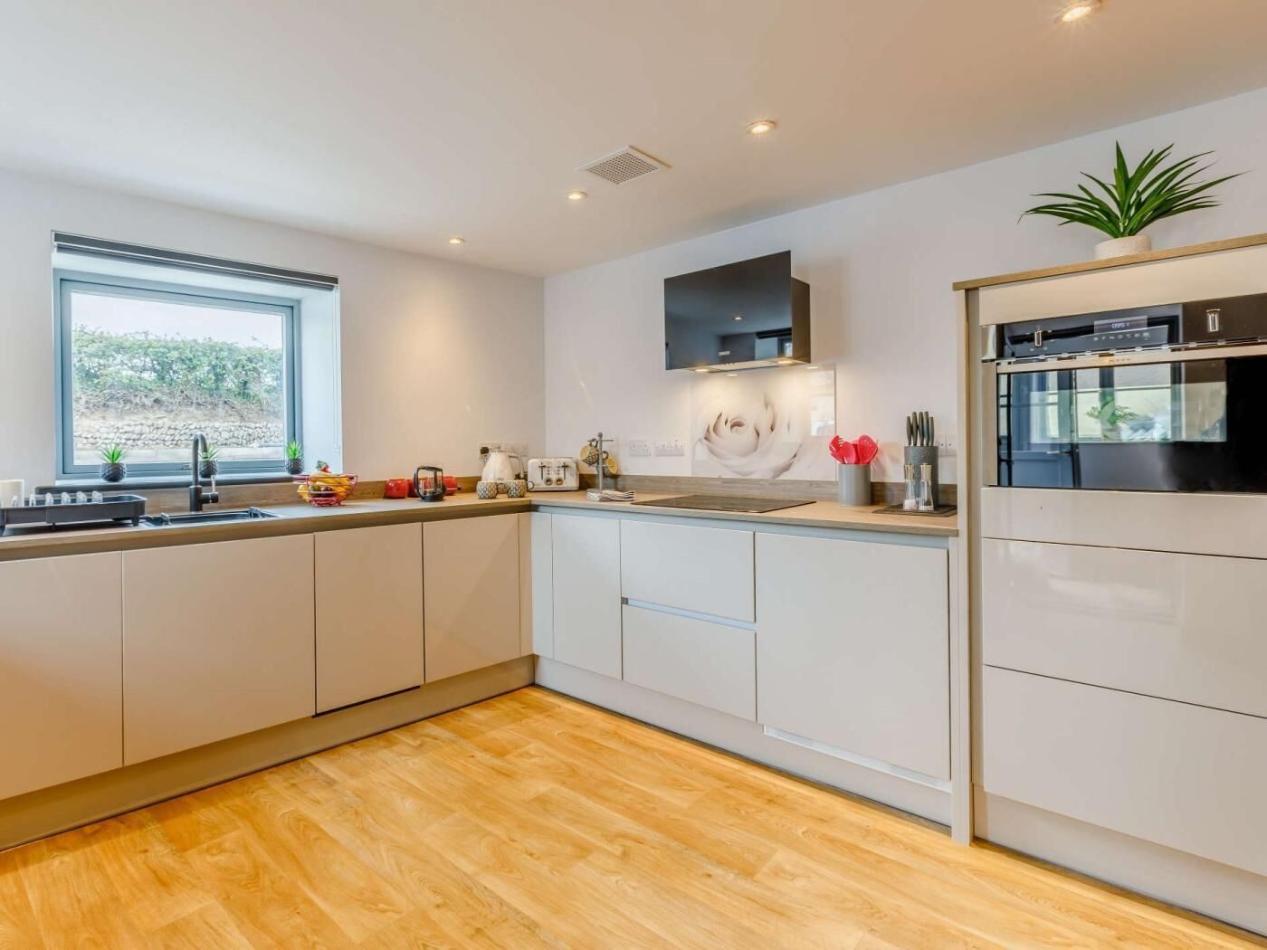 A modern kitchen with white cabinets, a built-in oven, and a window with a view of greenery.