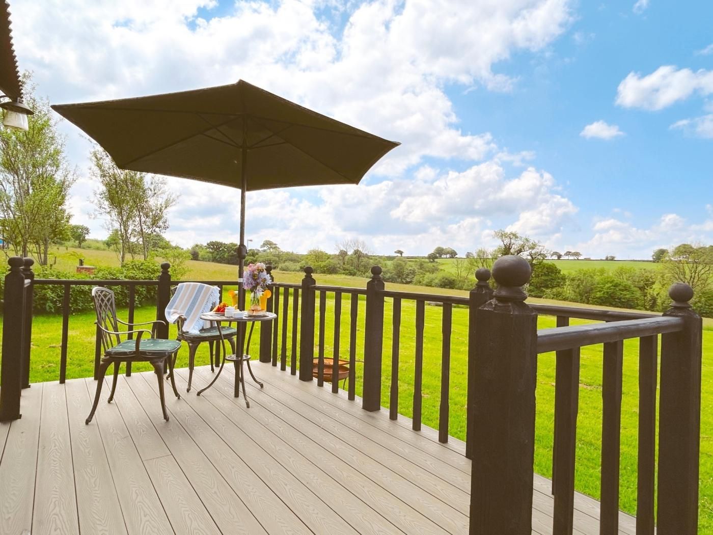A wooden deck with a table and chairs, an umbrella, and a view of a grassy field.