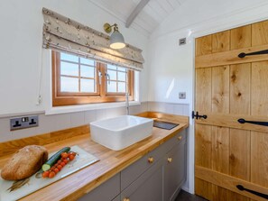 Eine Küche mit einer Holzausstattung, einem weißen Spülbecken, einem Fenster mit Vorhang und einer Tür mit Griff.