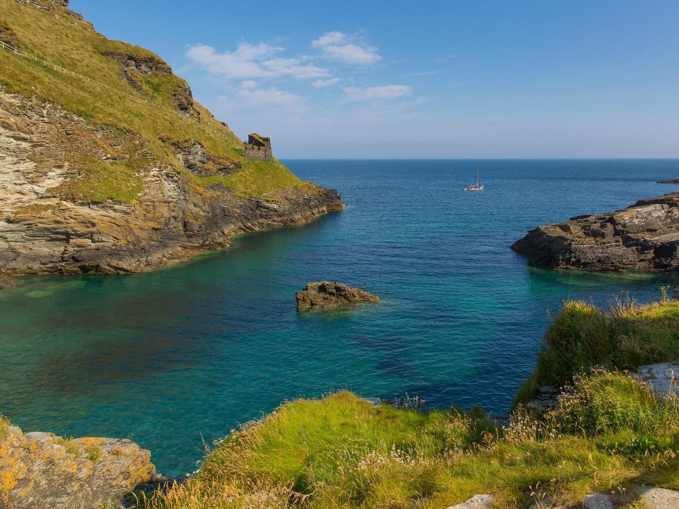 Un paysage côtier avec des falaises rocheuses, une eau d’un bleu limpide et un voilier.