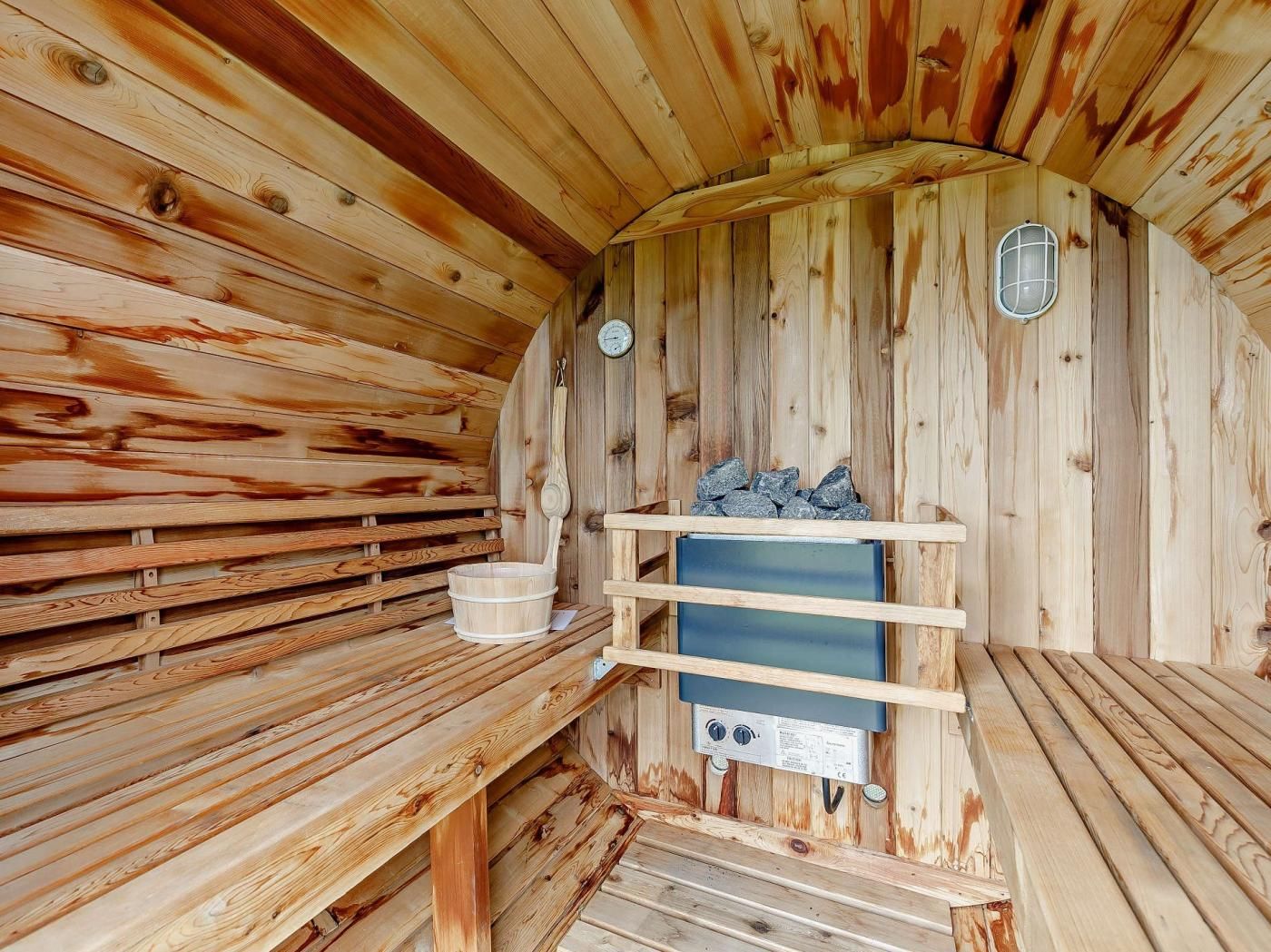 Uma sauna com paredes e bancos de madeira, um aquecedor e um prateleira de pedra.