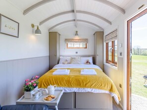 Ein Schlafzimmer mit Bett, Nachttisch mit einem Frühstücksangebot, einem Fenster mit Blick ins Freie und einer Wandleuchte.