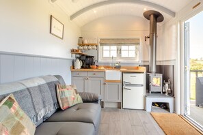 A compact kitchen with a built-in stove, a dining area with a table and chairs, and a sofa with a blanket. - 1 Bed in Beaworthy (oc-93267) (Ashwater)