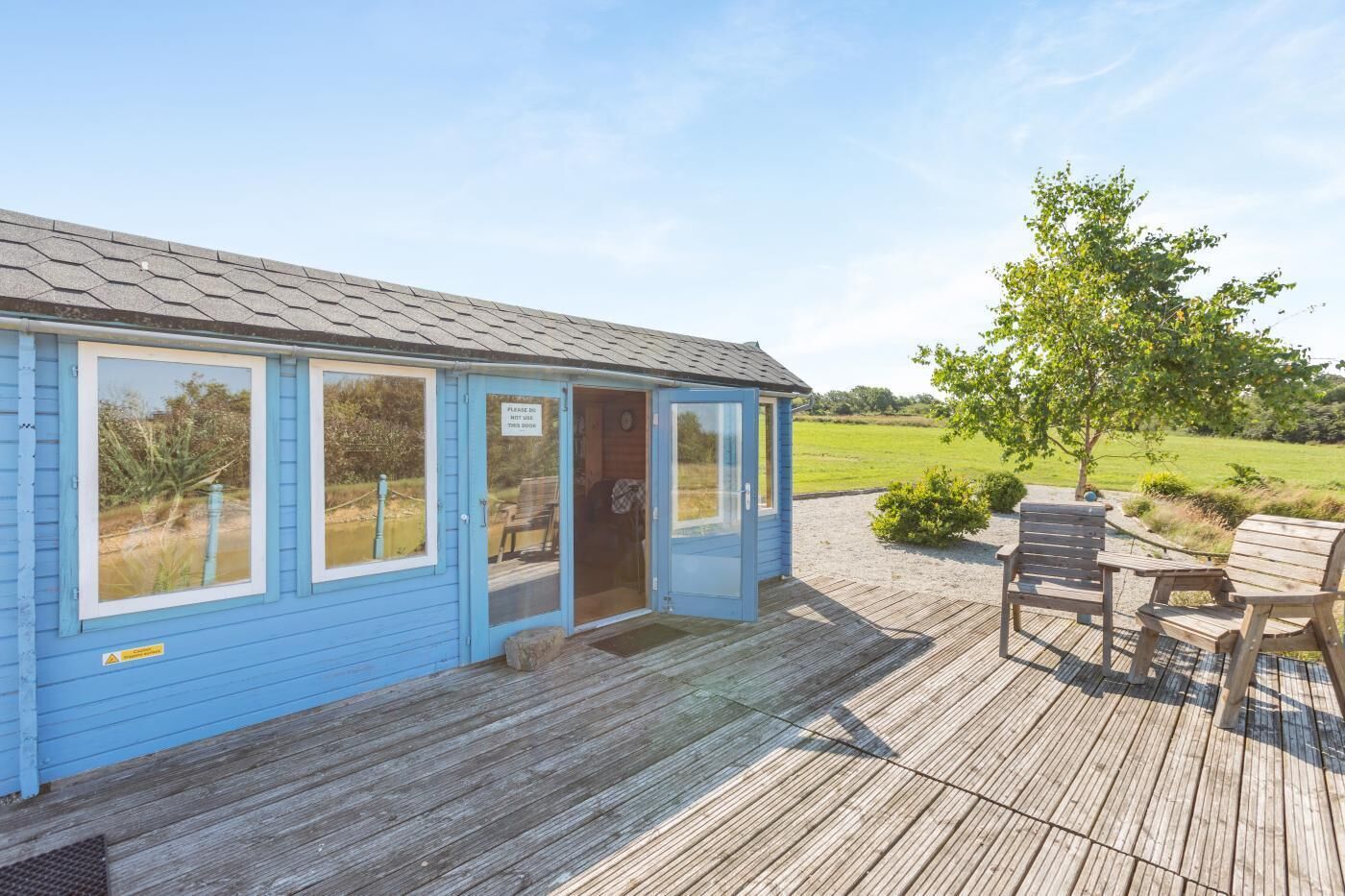 A blue cabin with a wooden deck and a view of the countryside.
