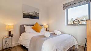 A neatly arranged bedroom with a bed, two bedside lamps, a window with a view, and a painting on the wall. - 2 Bed in Colchester (oc-95941) (East Bergholt)