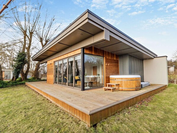 A modern house with a wooden deck, glass sliding doors, a hot tub, and a covered patio area.