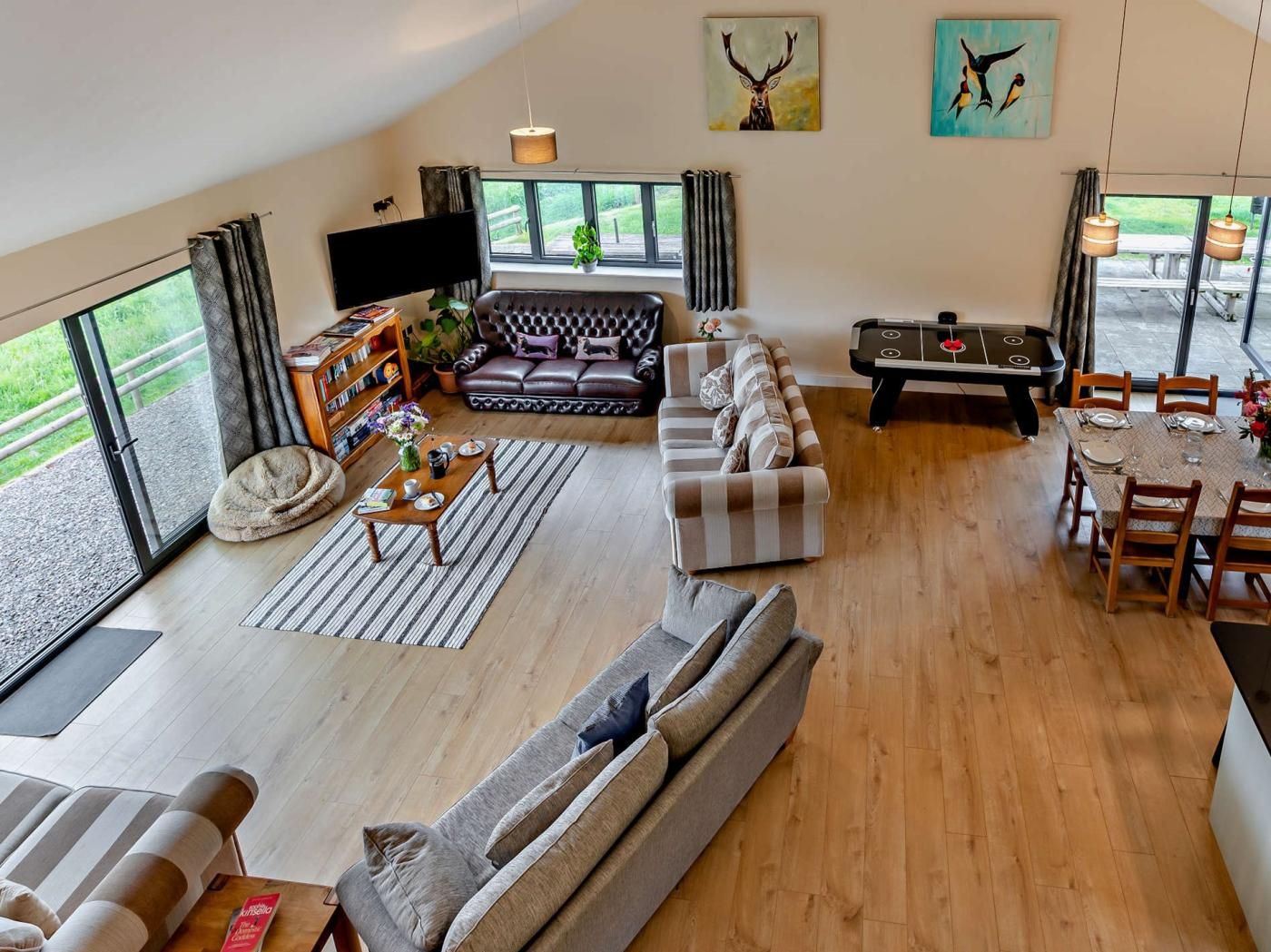 A spacious living area with a large sofa, a dining table set for four, and a flat-screen TV mounted on the wall.
