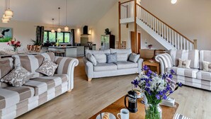 A spacious living area with a high ceiling, a kitchen in the background, and a staircase leading to an upper floor. - 5 Bed in Dulverton (oc-87003) (Morebath)
