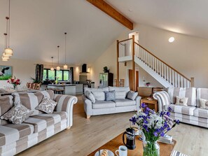 A spacious living area with a high ceiling, a kitchen in the background, and a staircase leading to an upper floor. - 5 Bed in Dulverton (oc-87003) (Morebath)