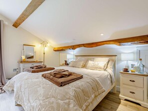 A bedroom with a large bed, bedside tables, a mirror, and a wooden ceiling beam.