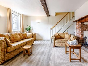 Ein Wohnzimmer mit zwei gemusterten Sofas, einem kleinen Holzschemel, einem Tisch mit einer Auflage und einer Treppe zu einem Kamin aus Ziegeln.