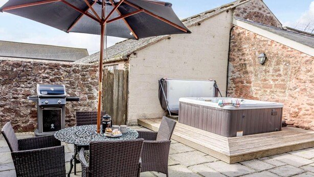Eine Terrasse mit Tisch, Stühlen, Grill, Whirlpool und einer Steinmauer.