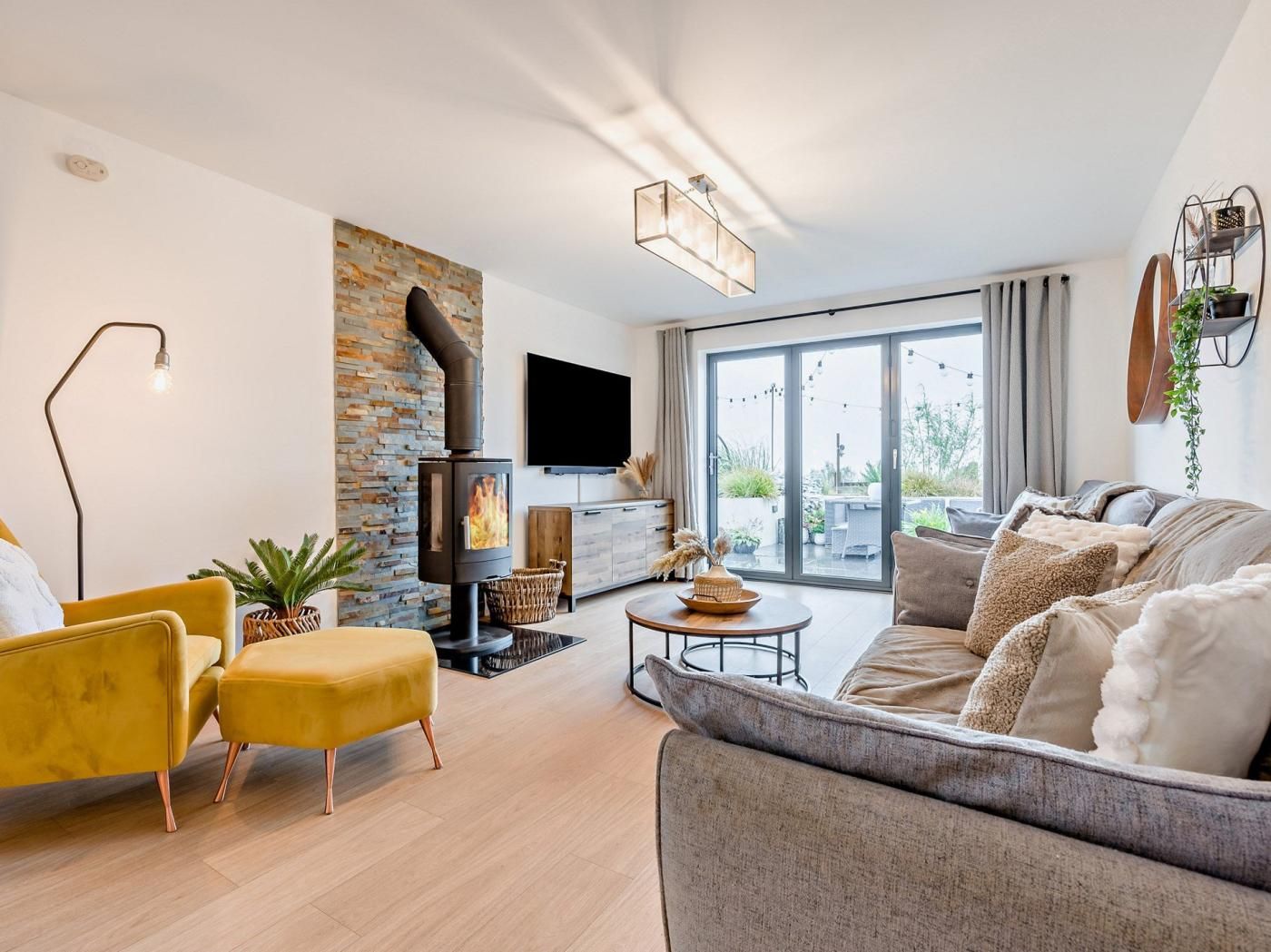 Un salon moderne avec une cheminée, un canapé, un fauteuil jaune et un téléviseur.