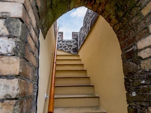 Un escalier, avec un mur en pierre d’un côté et un mur uni de l’autre, qui mène à un niveau supérieur.