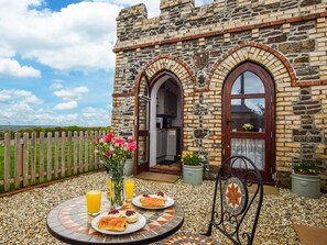 A stone building with a wooden fence, a tiled patio, and a table with food and drinks. - 1 Bed in Okehampton (oc-78799) (Hatherleigh)