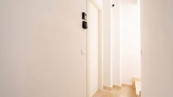 Un couloir étroit avec une porte sur la gauche, un interrupteur et un interphone fixé au mur.