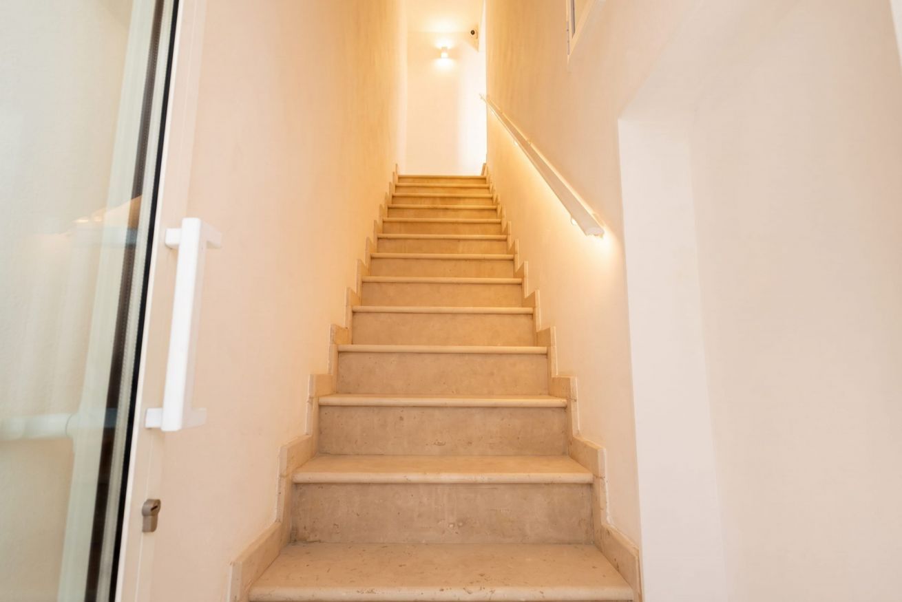 Un escalier avec une rampe, menant à un palier doté d’un luminaire.
