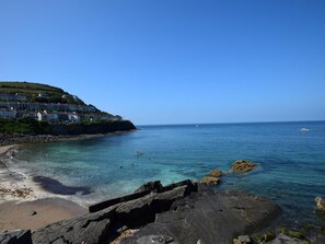 A coastal scene with clear water, rocky shoreline, and a hillside with buildings. - 3 Bed in New Quay (oc-83998) (New Quay)