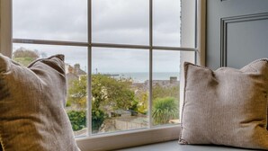 A window seat with two pillows, a view of a coastal area, and a stone wall. - 3 Bed in New Quay (oc-83998) (New Quay)