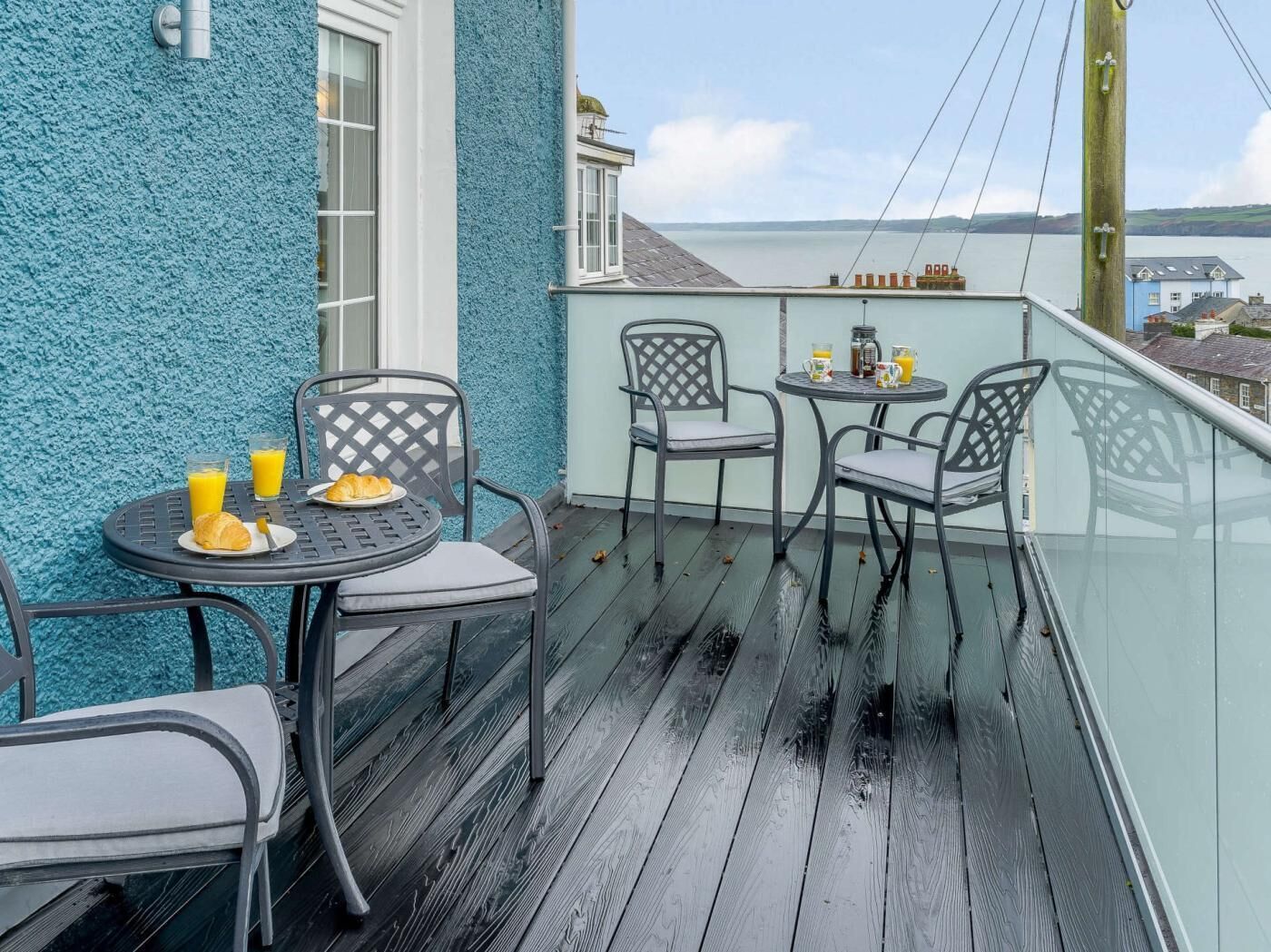 Ein Balkon mit Meerblick, ausgestattet mit einem Tisch mit Frühstücksangeboten, zwei Stühlen und einem kleinen runden Tisch mit Getränken.