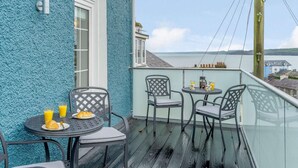A balcony with a view of the sea, featuring a table with breakfast items, two chairs, and a small round table with drinks. - 3 Bed in New Quay (oc-83998) (New Quay)