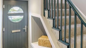 A dark wooden door with a window, a white wall, and a staircase with beige carpet and black railings. - 3 Bed in New Quay (oc-83998) (New Quay)