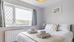 Quarto com cama, janela com cortinas, radiador e um quadro na parede.
