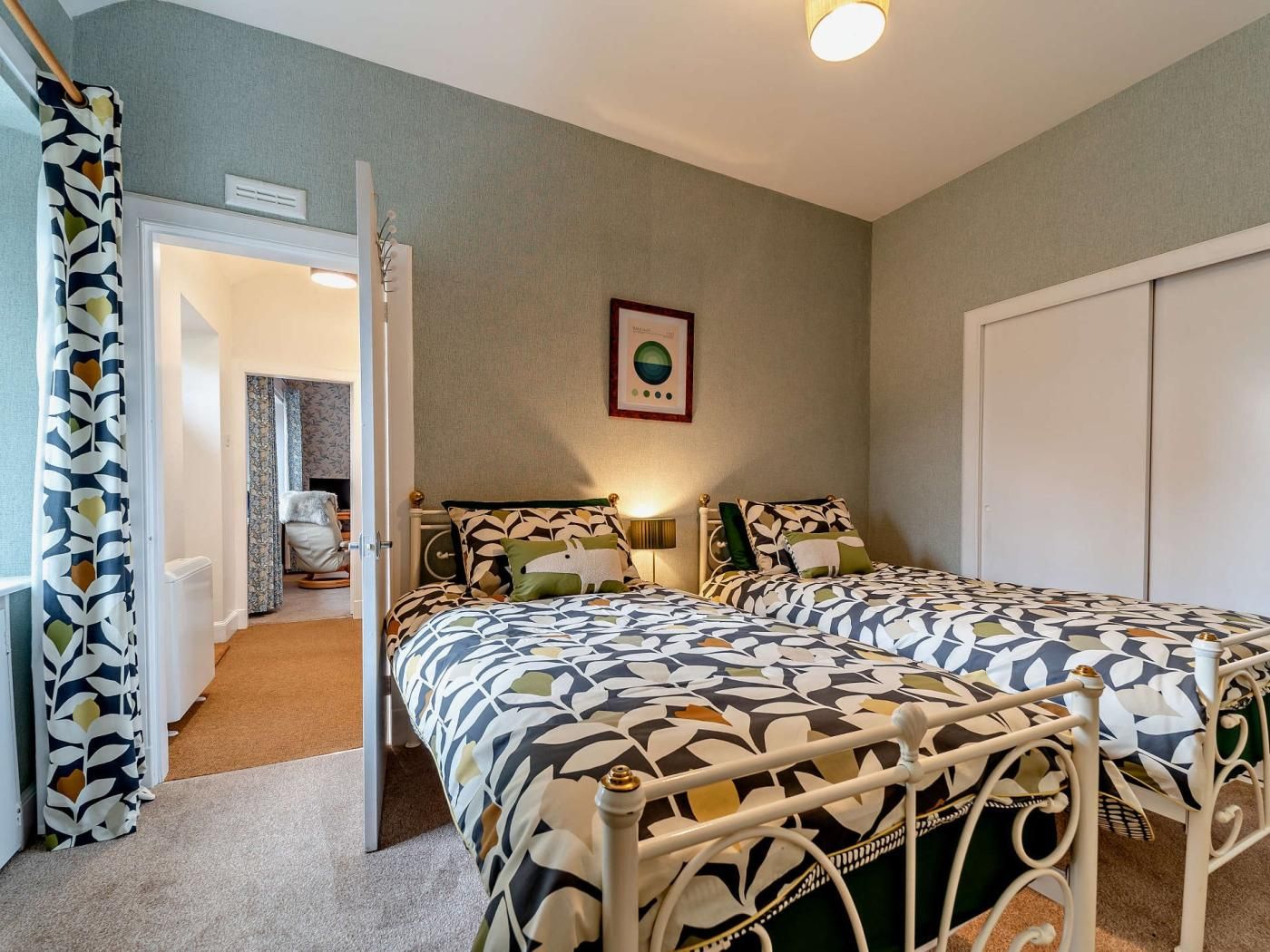 A bedroom with two beds, a door leading to another room, and a wall-mounted light fixture.
