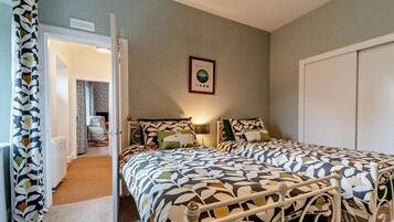 A bedroom with two beds, a door leading to another room, and a wall-mounted light fixture.
