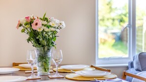 Uma mesa de jantar posta com pratos, copos e um vaso de flores.