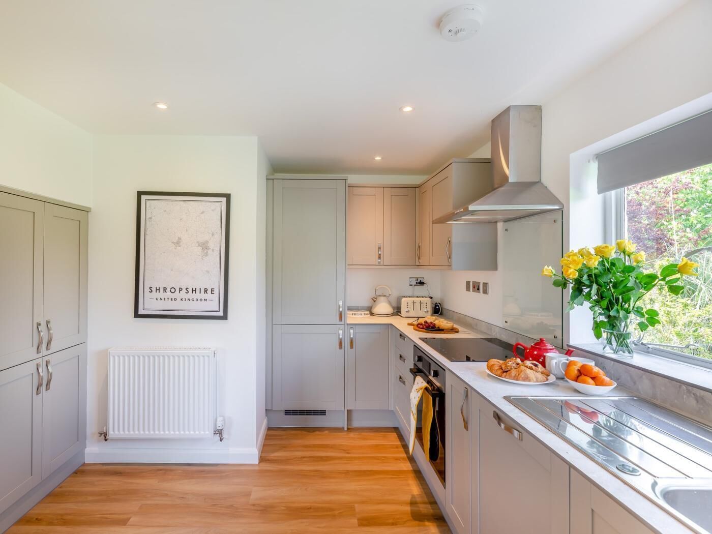 A modern kitchen with white cabinets, a built-in oven, a window with a view, and a framed map on the wall.