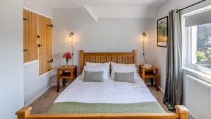 Um quarto com cama de madeira, duas mesas de cabeceira, luminária pendente, janela com cortinas e armário fixado na parede.