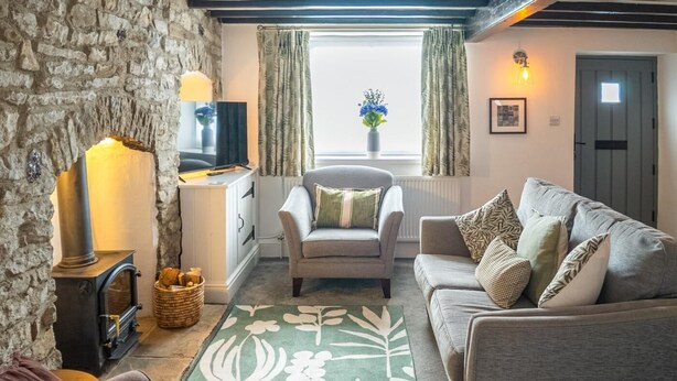Ett mysigt vardagsrum med en vägg av sten, en öppen spis, en soffa, en tv och ett fönster med gardiner.